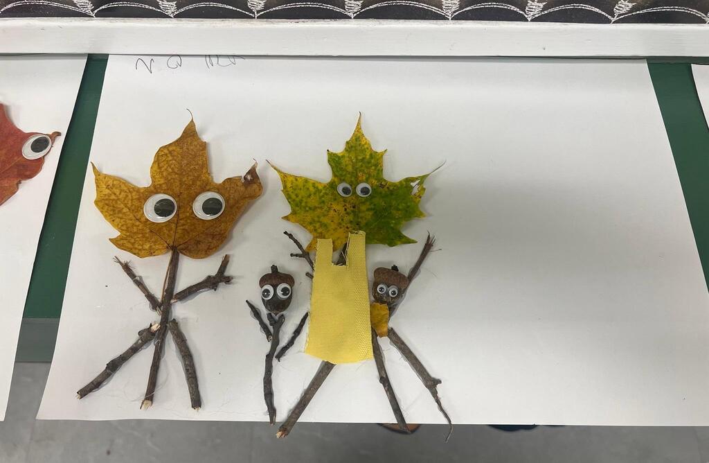 Student artwork of three figures created using leaves, sticks, acorns with googly eyes, and yellow mesh fabric.