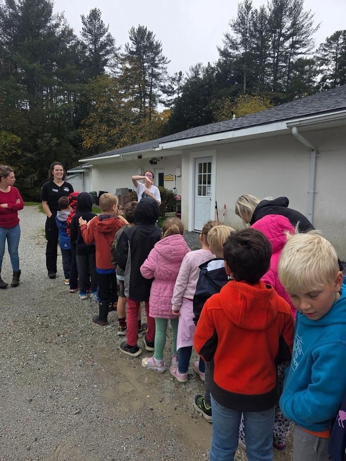 A line of students waiting outside a shelter building while an instructor speaks to them.