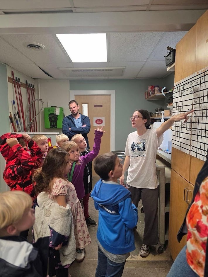 An animal shelter staff member points to an informational white board while teaching a group of visiting students.
