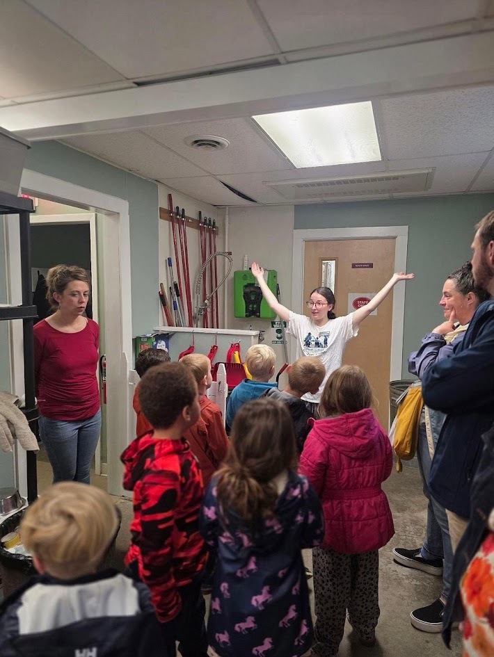 An instructor speaking with arms outstretched to a group of students during a facility tour.