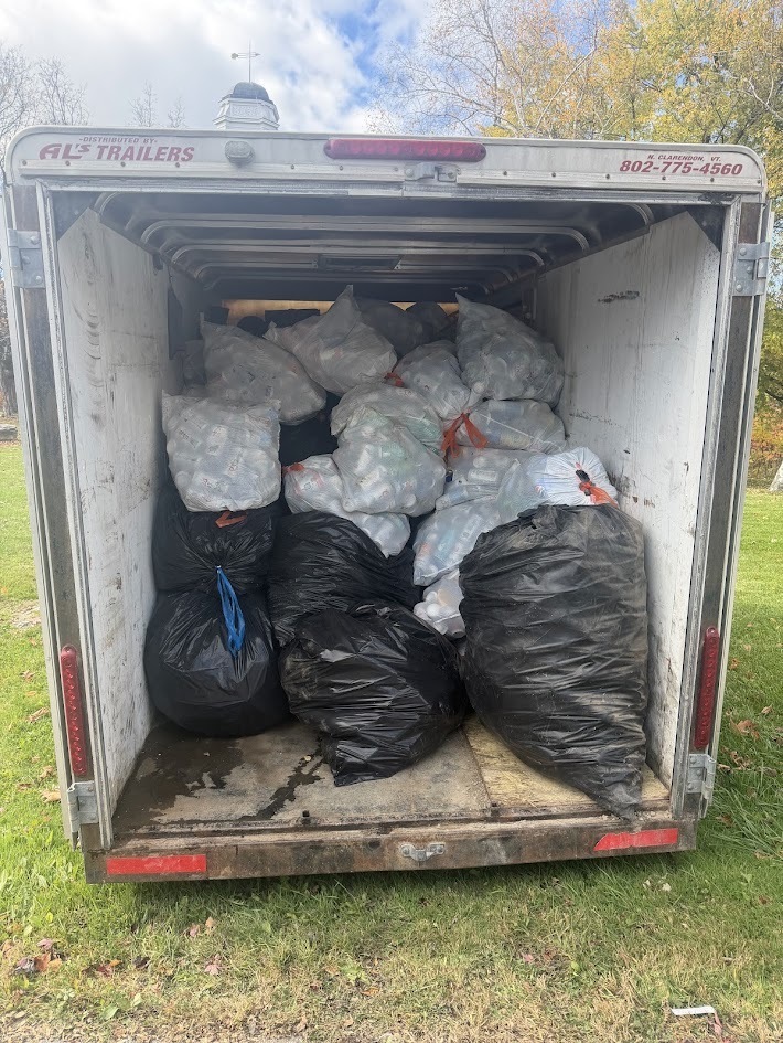 The interior view of an open cargo trailer packed full of clear and black trash bags filled with recyclable cans and bottles.
