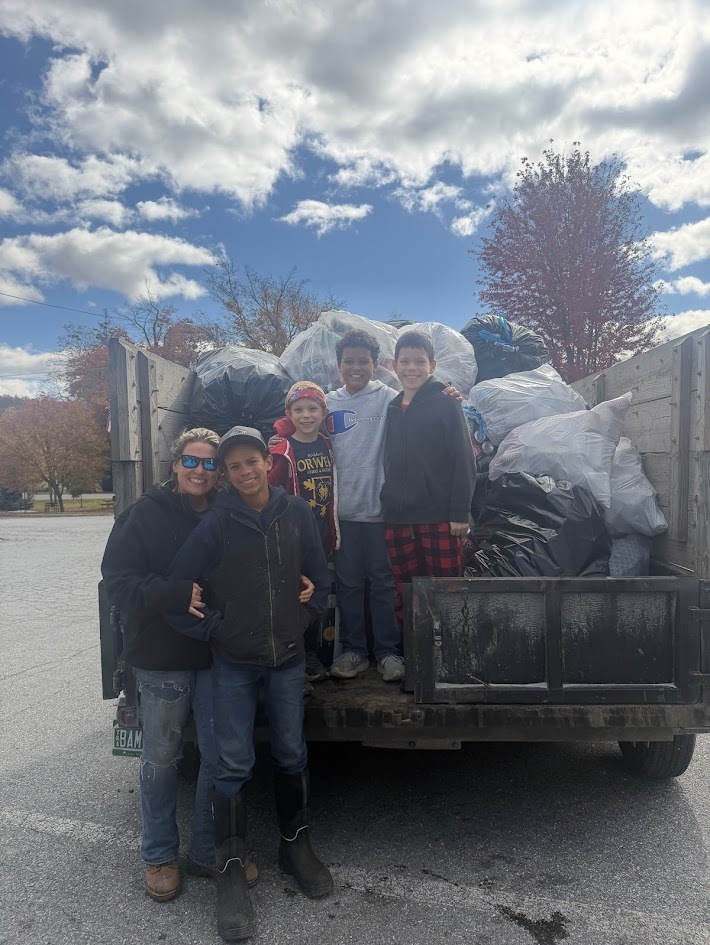A woman and four young boys standing and smiling in front of the back of a flatbed truck filled with bags of donated items for a collection drive.