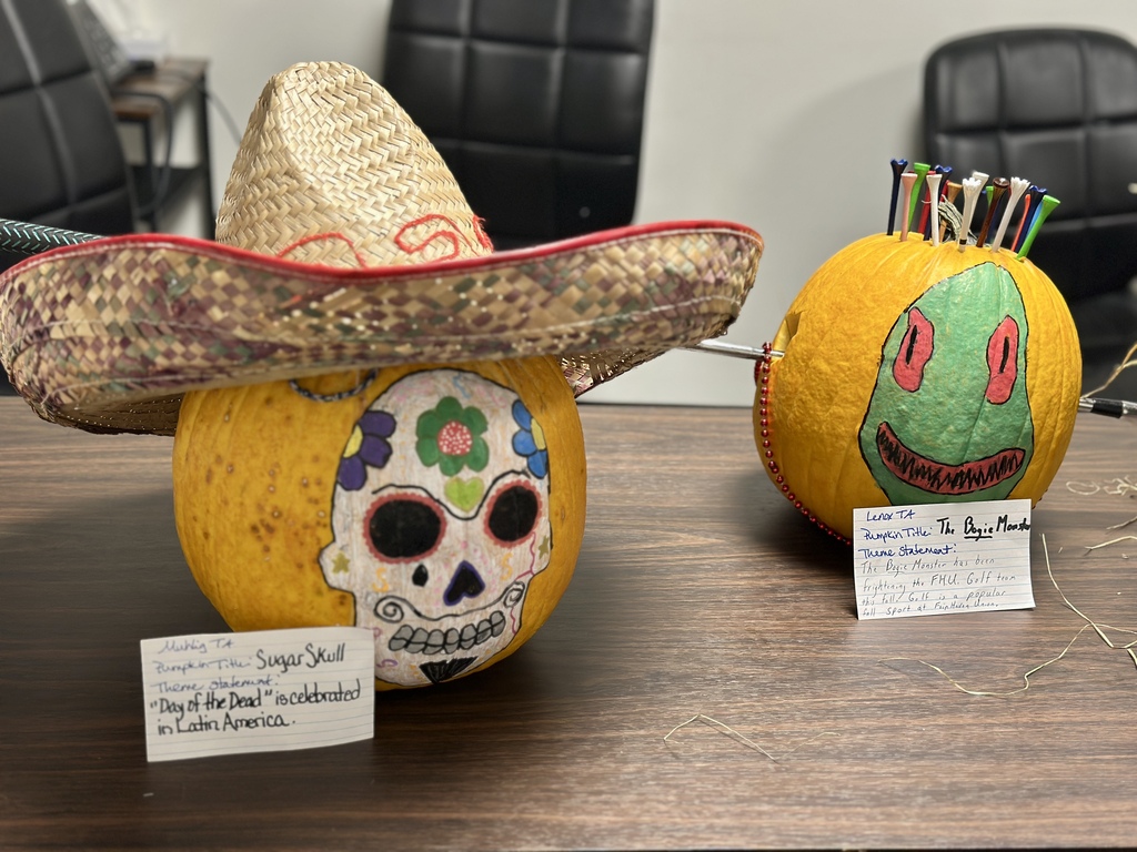 Two decorated pumpkins side-by-side on a wooden table: a "Sugar Skull" pumpkin wearing a straw sombrero and a golf-themed "Bogie Monster" pumpkin stuck with golf tees.