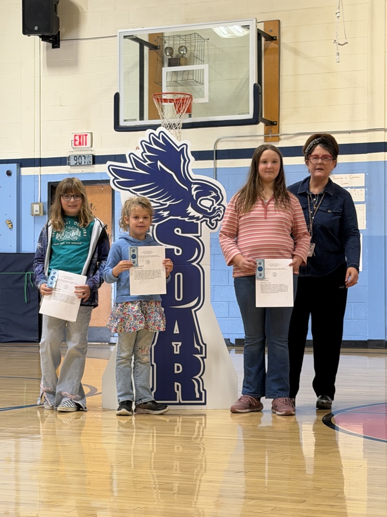 Three female students holding award certificates and vouchers pose with a teacher beside the FHGS SOAR sign.