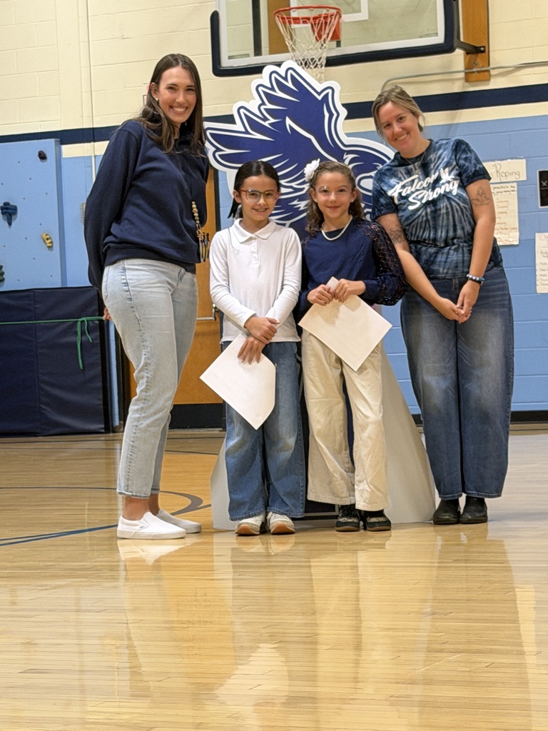 Two female students holding SOAR award papers pose with two smiling teachers around the school mascot cutout.