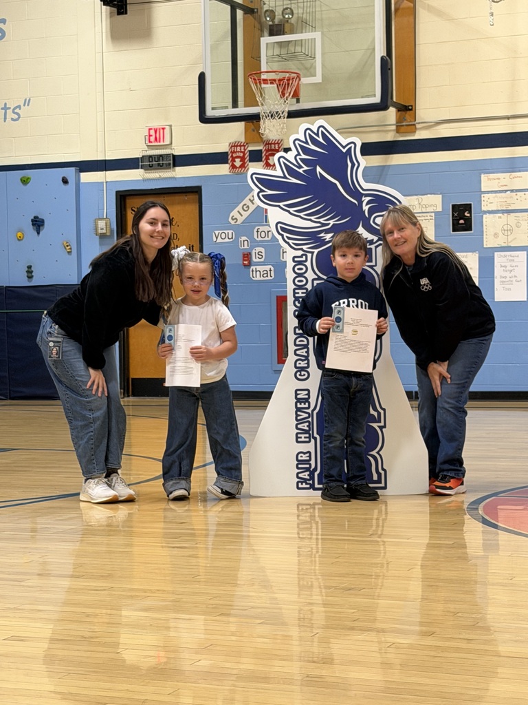 Two students holding certificates and award vouchers pose with two teachers around the Fair Haven Grade School SOAR cutout.