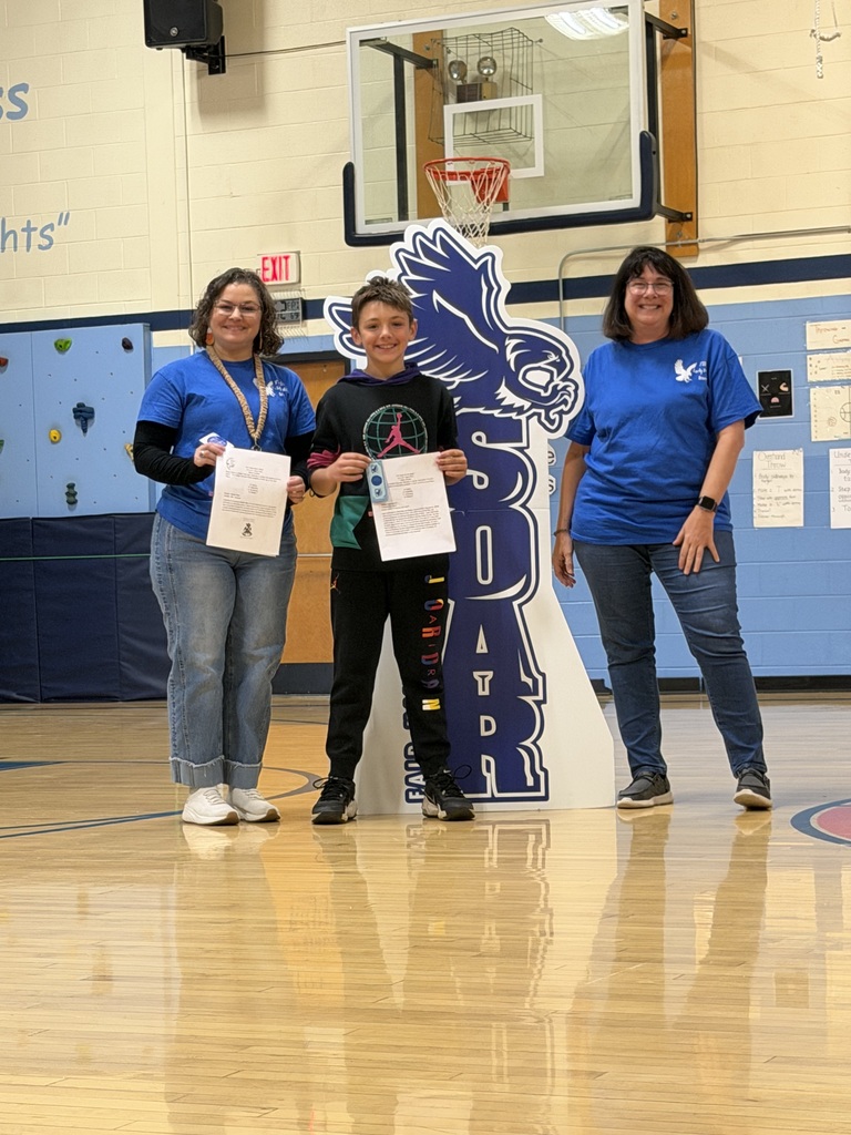 A student holding an award paper poses with two staff members wearing blue Falcon shirts beside the SOAR cutout.