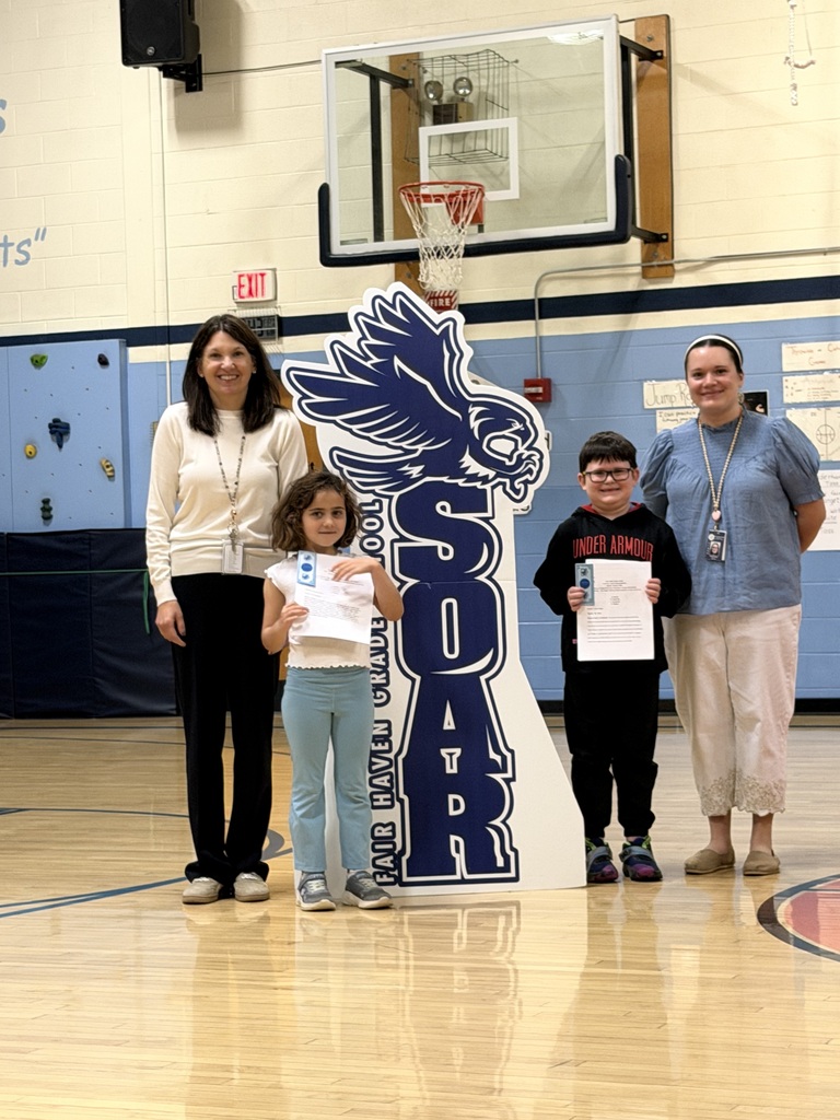 Two elementary students proudly holding SOAR certificates pose alongside two staff members in the school gym.