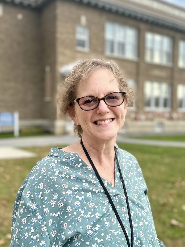 Photo of next year's FHGS Principal, standing in front of the school building, smiling wearing a green floral blouse