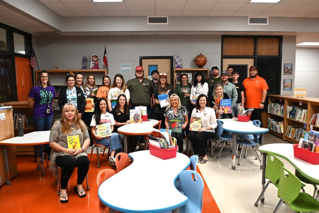 A group of people pose for a picture in a classroom with tables, chairs, and bookshelves.