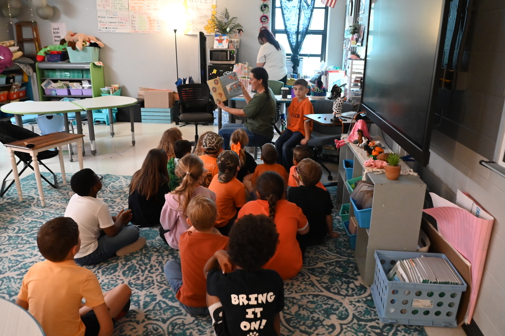 A teacher reads to young children sitting in a circle on the floor in a classroom.