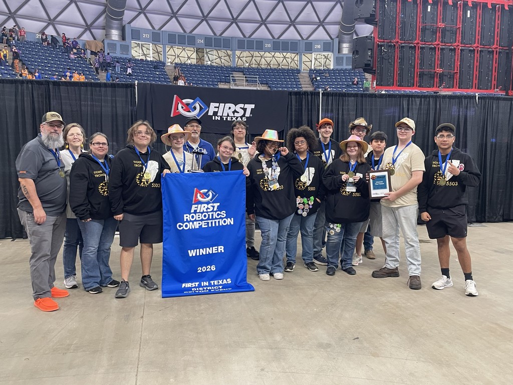 Group of people stand behind a banner reading "FIRST Robotics Competition Winner" in front of a stadium.