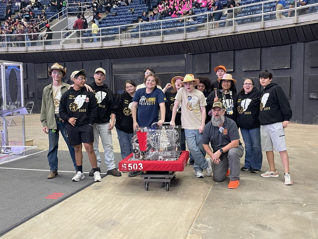 A group of people stands around a red cart in an indoor sports facility, some wearing hats and sneakers.