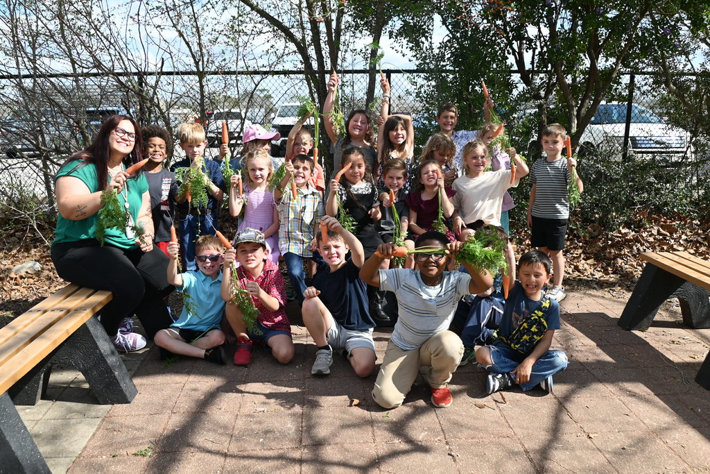 teacher and students holding up the carrots they picked in the garden