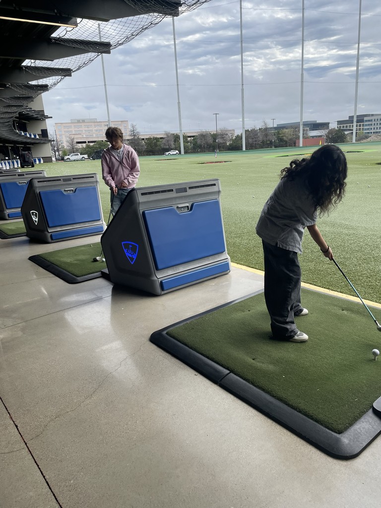 Two people practicing golf in an indoor range. One is holding a club and preparing to hit.