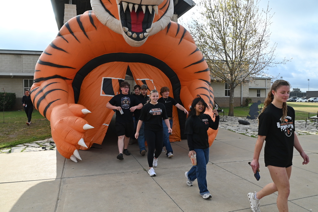 A group of people in black t-shirts walk past a large inflatable tiger in front of a building.