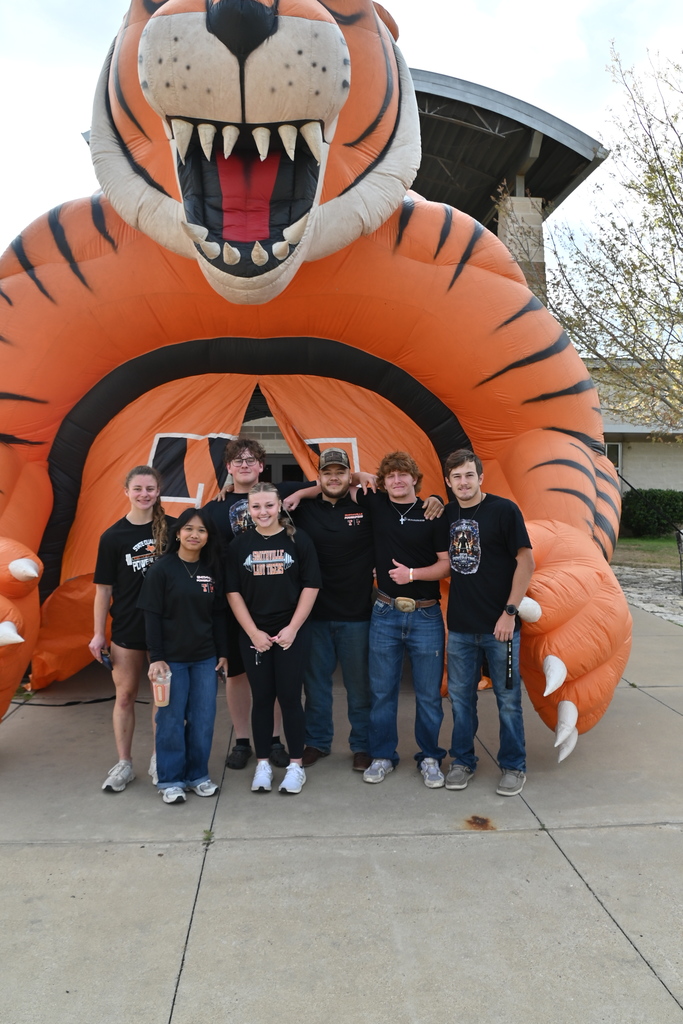 A group of people stand in front of a large inflatable tiger mascot. 