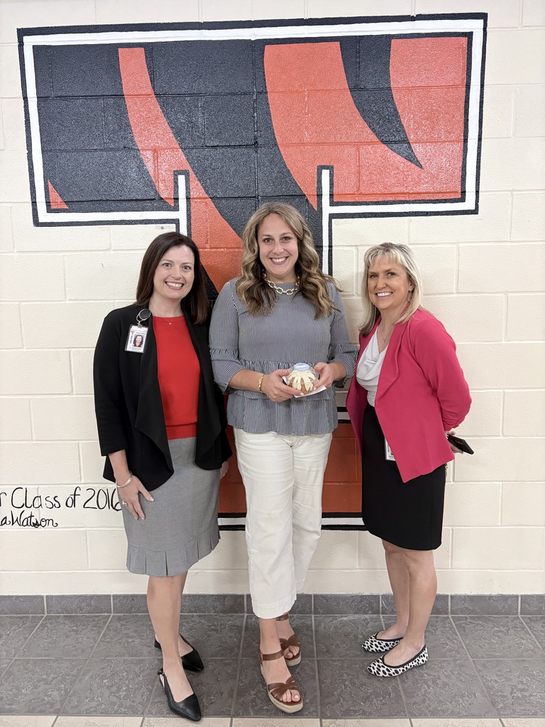 three ladies dressed in business attire; the middle lady is holding a small cake