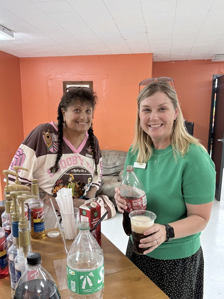 two ladies, one holding a drink cup, smile at the camera