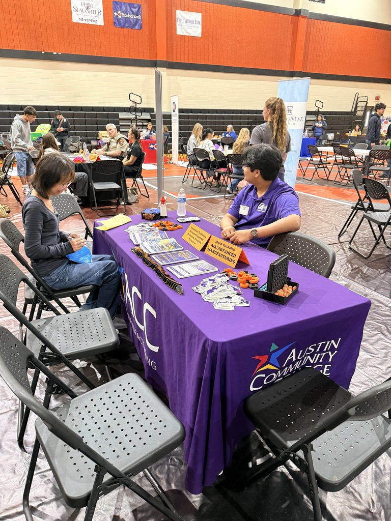 Two people sit at a table covered with a purple tablecloth. A sign reading "Austin Community College" is visible.