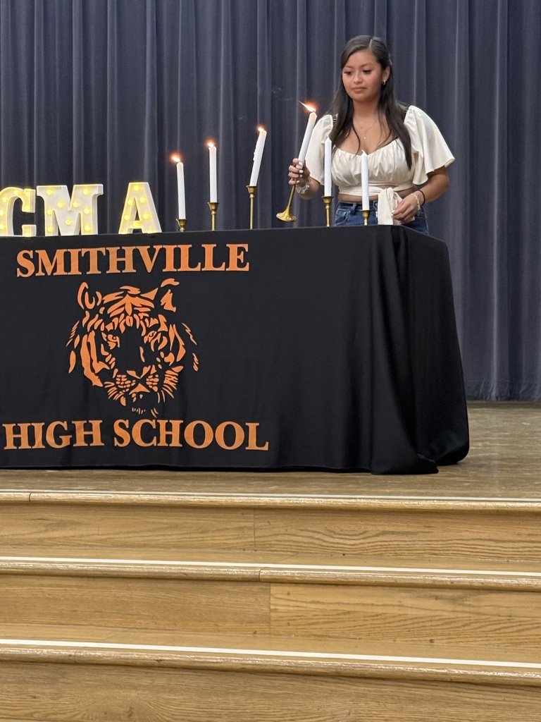 A woman standing at a table with a black cloth featuring the words "Smithville High School" and a tiger logo.