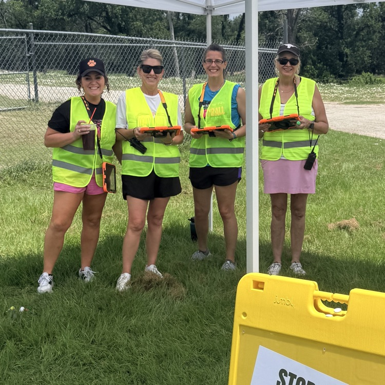 four women in yellow vests stand under a tent