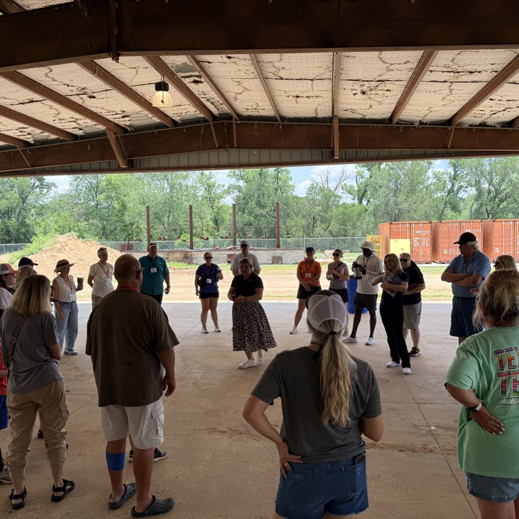 a group of people stand in a circle listening to a woman