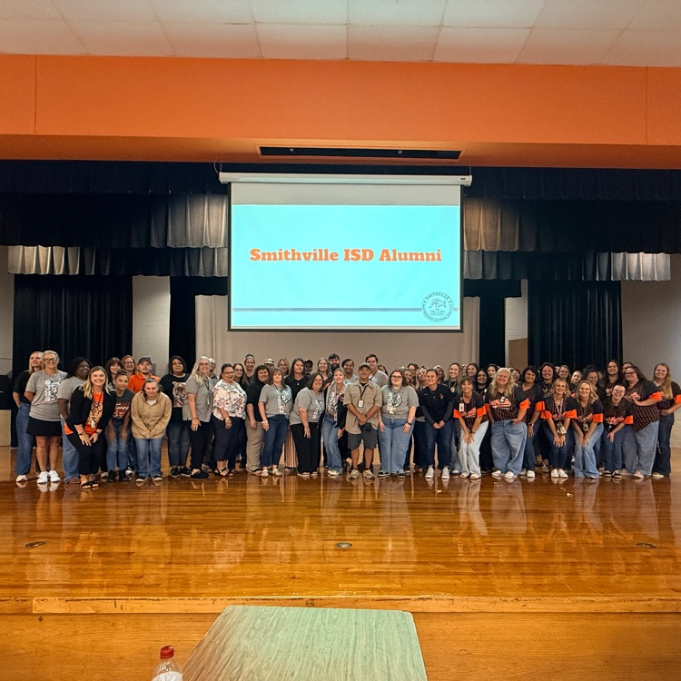 a group of people pose for a photo under a sign that says “Smithville ISD alumni"