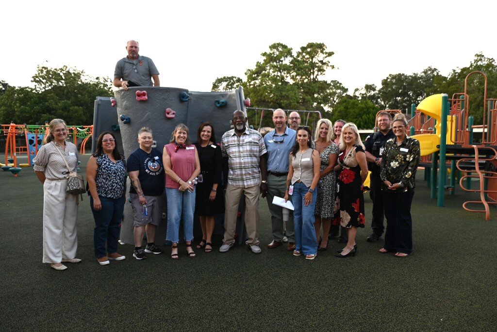 A group of people, some wearing hats, standing in front of playground equipment in a park.