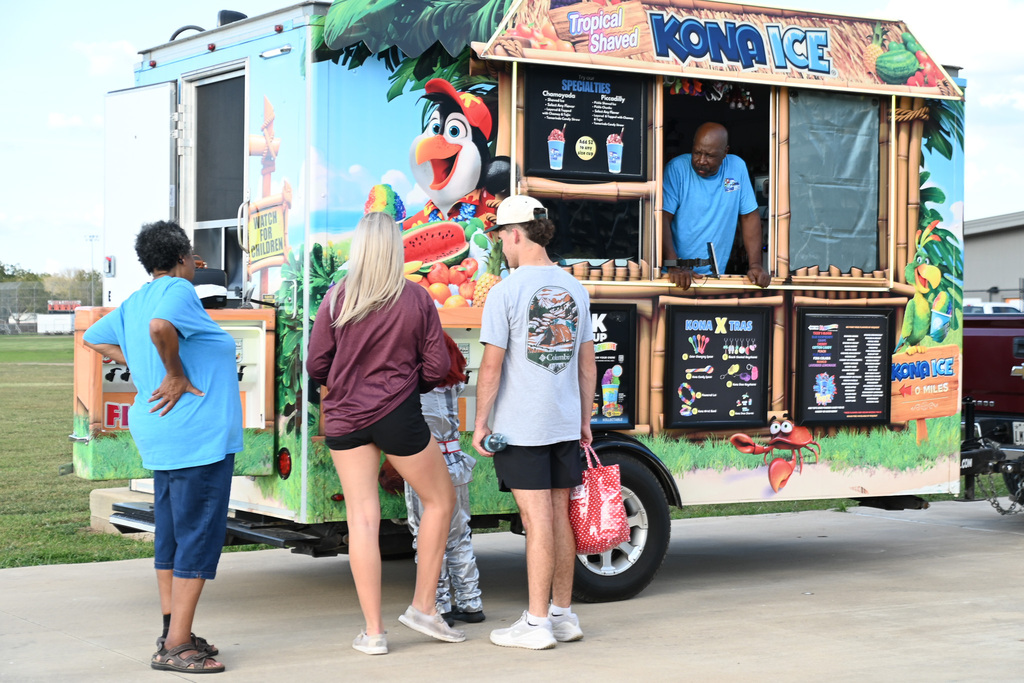 People standing by a food truck with a tropical design and an ice cream vendor inside.
