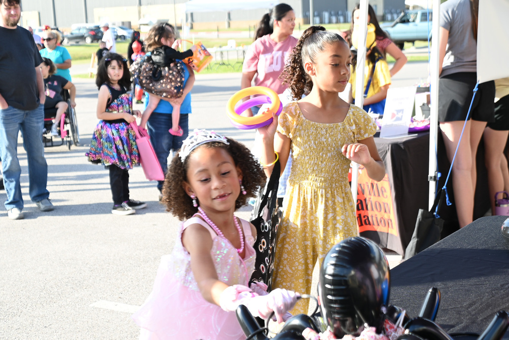 Two girls in colorful dresses; one holding a colorful balloon and the other holding a toy.