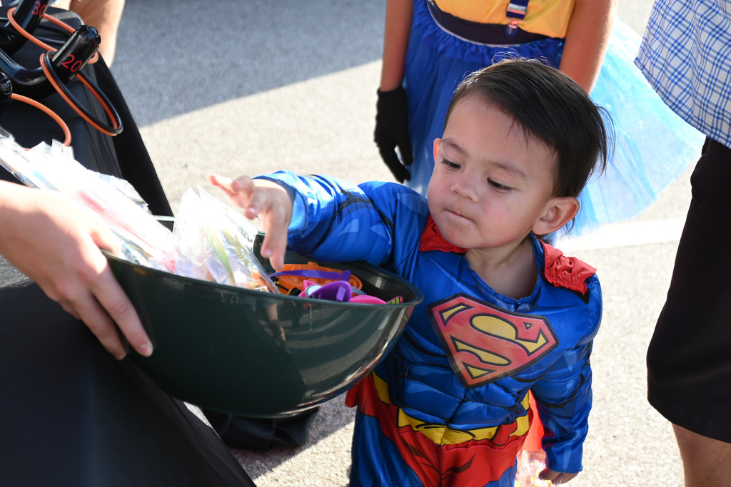 A young boy in a Superman costume holds a green bowl, reaching into it with his right hand.