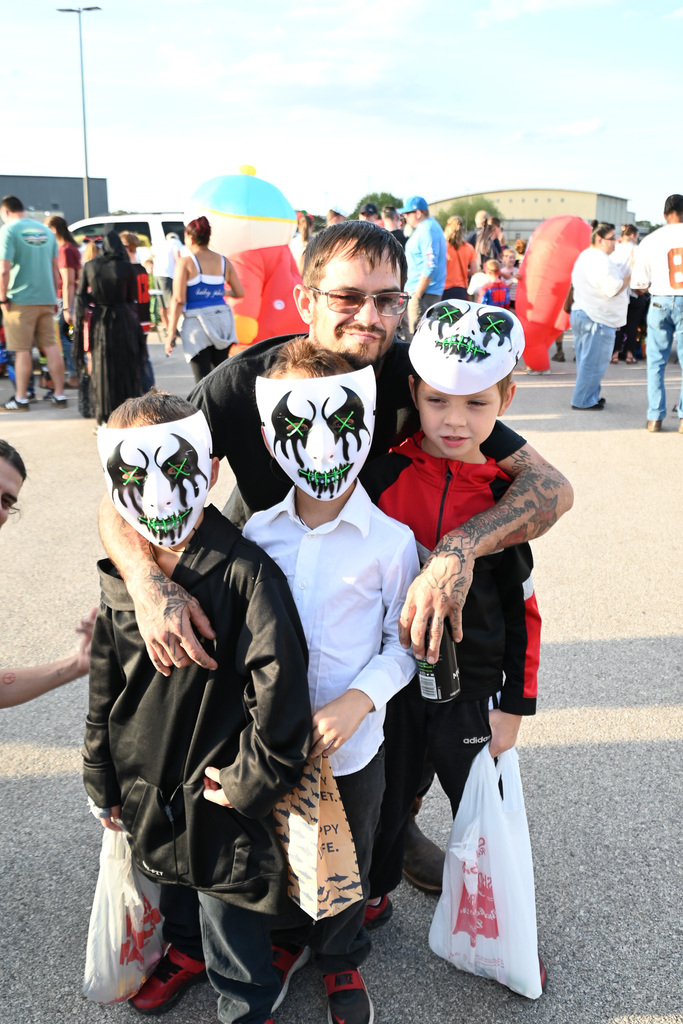 Three children with masks and a man hold bags while standing in a parking lot.