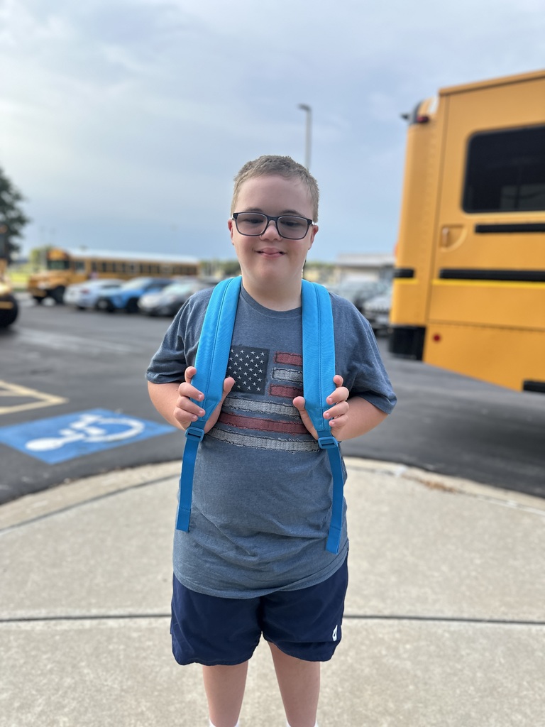 A high school boy poses in front of the school with his backpack on