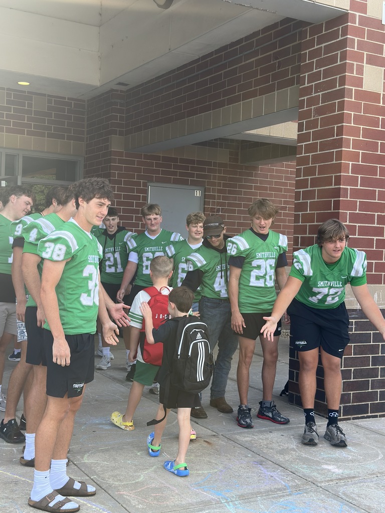 Football players line up in front of the school to greet elementary students