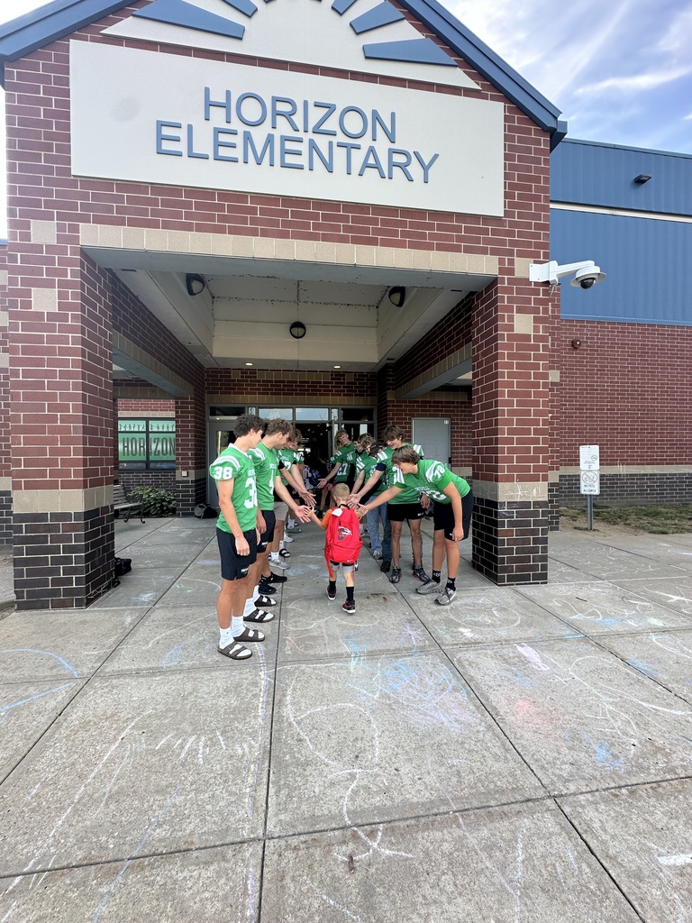 Football players line up in front of the school to greet elementary students