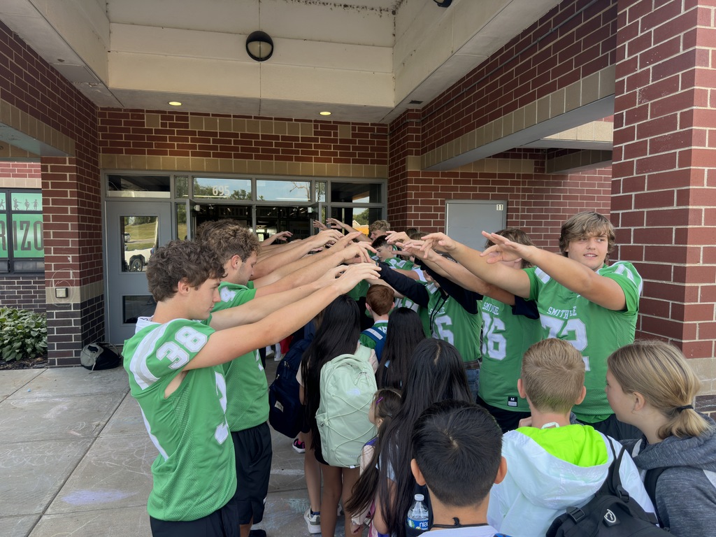 Football players line up in front of the school to greet elementary students
