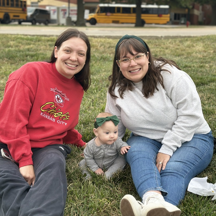 teachers and a baby sitting in the grass at the tailgate