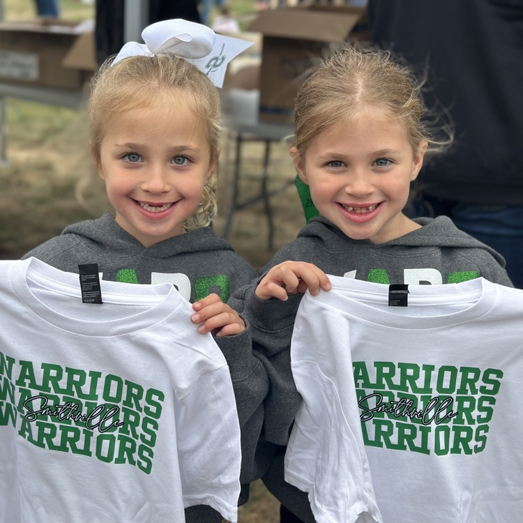 two little girls holding their warrior T-shirts up to them