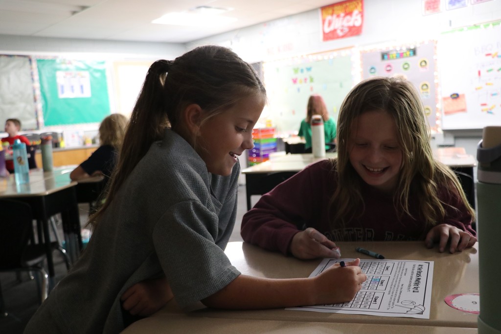Two 4th grade girls play a multiplication dice game at their desks