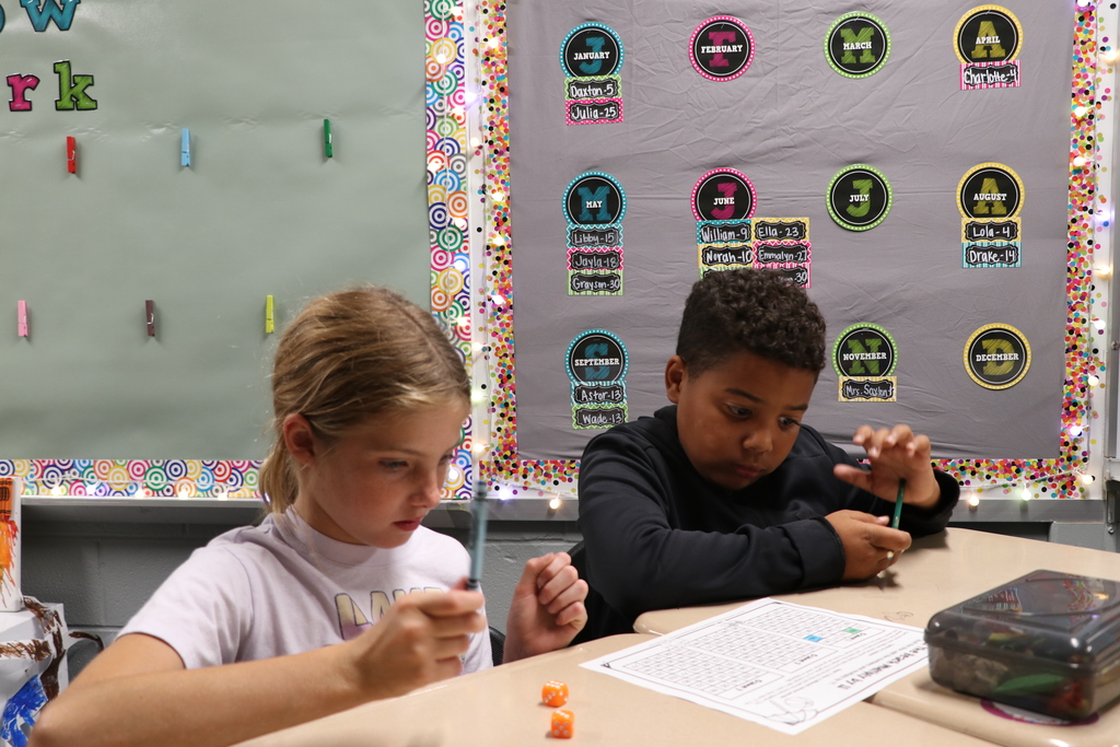 Two 4th graders play a multiplication dice game at their desks