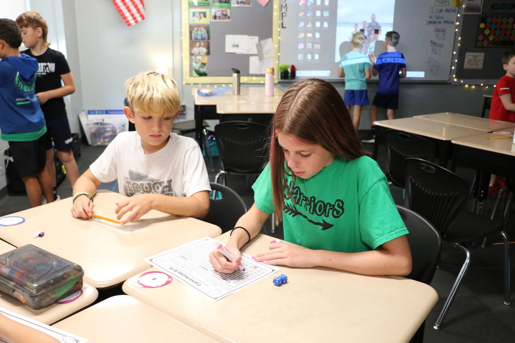 Two 4th grade girls play a multiplication dice game at their desks