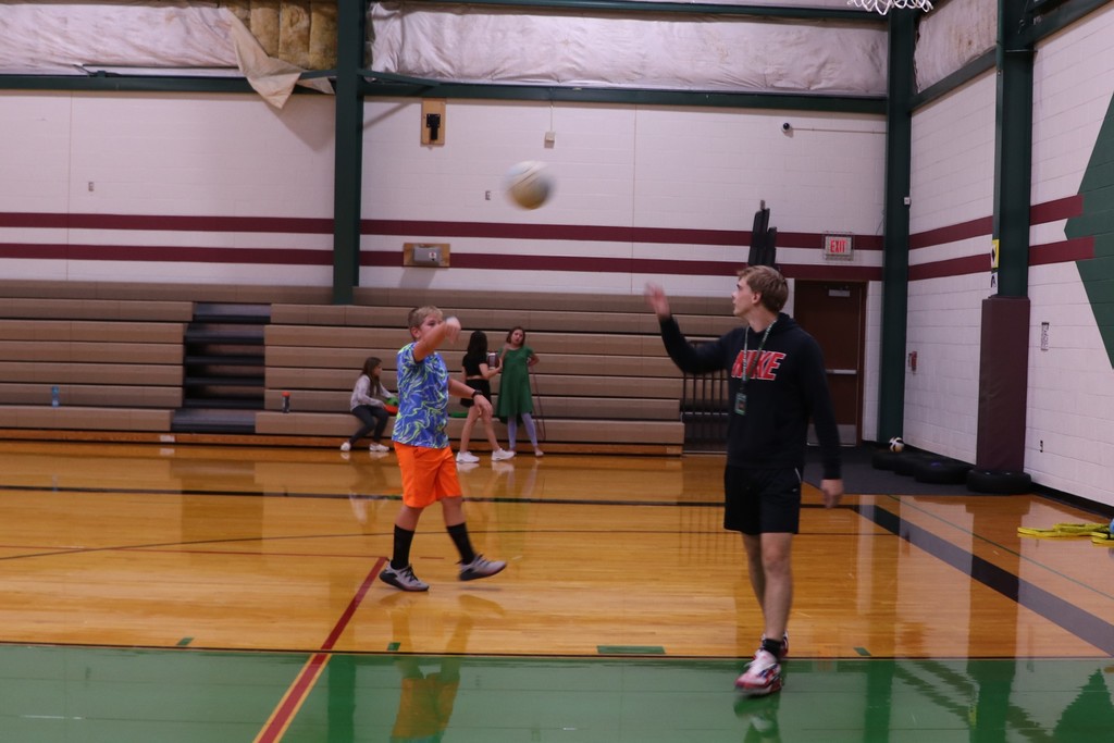 An elementary student is throwing a basketball to high school cadet teacher