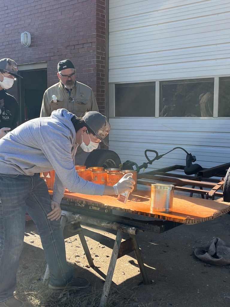 A student spray paints his tin can jack-o-lantern with orange spray paint.