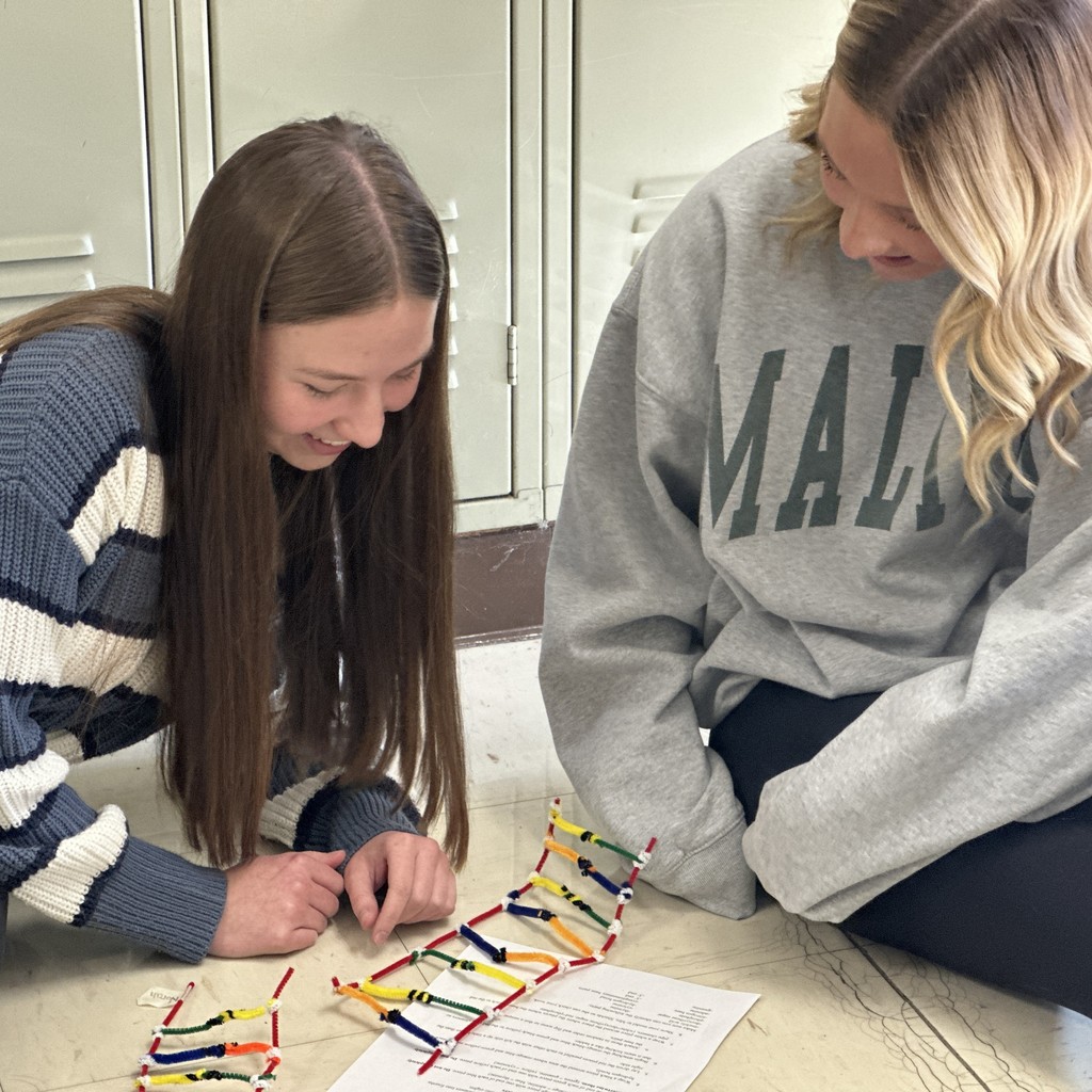 Two students sit on the floor and read the instructions to build a DNA model