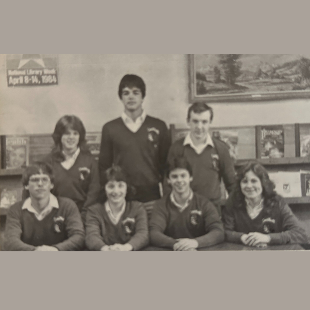 Seven students who made up the 1984 Academic Bowl team pose for a group photo in a library.