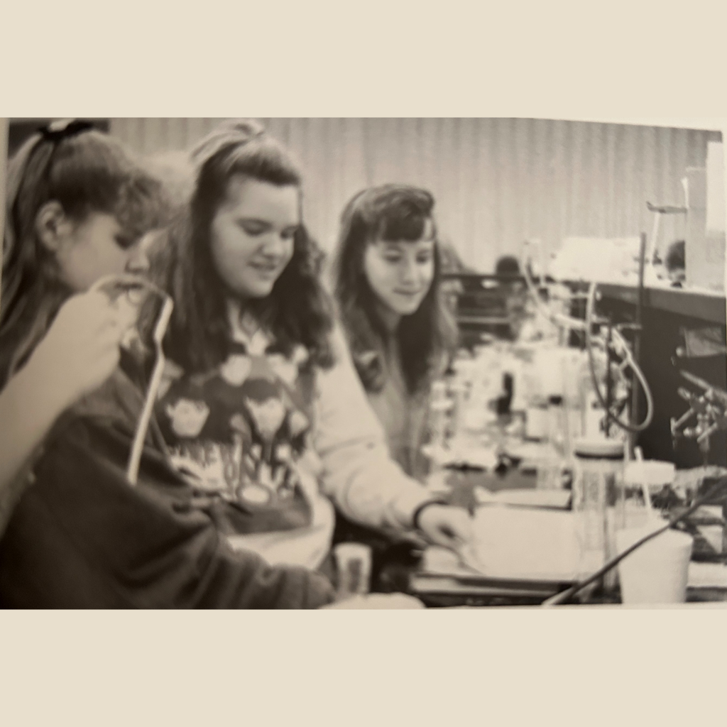 High School students sit at a lab table in a chemistry class with beakers and other supplies in front of them on the table.