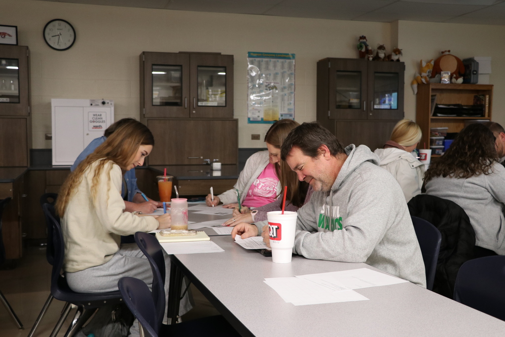 Teachers sit at a table on write while being timed.