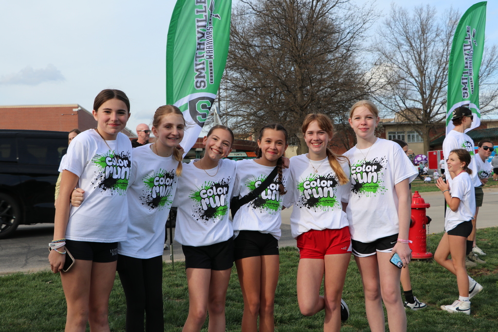 Six middle school aged girls wrap their arms around each other to pose for a picture. they are wearing Color Run shirts.