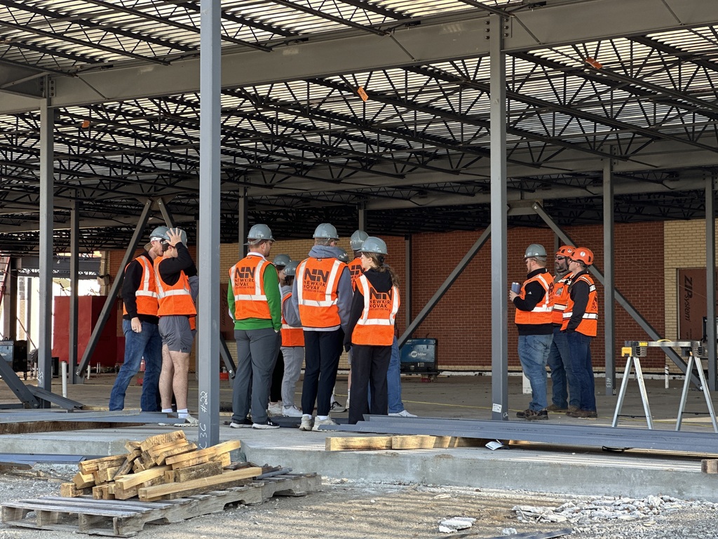 High School students dressed in orange vests and hard hats visit the construction site of the high school.